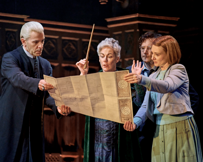 Cast on stage. Draco, Harry, Ginny & actress stare at a map.